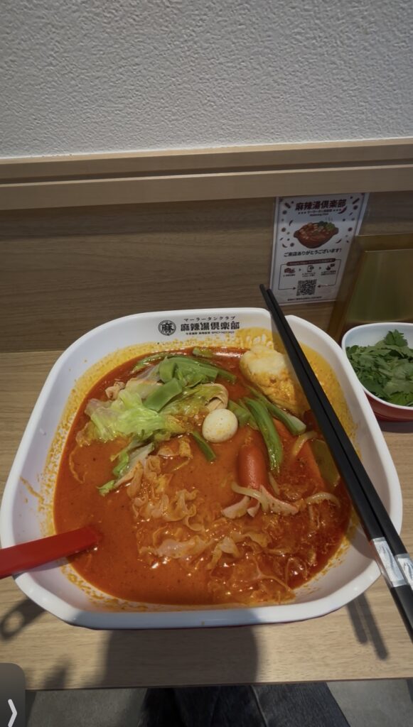麻辣湯倶楽部 船橋店で実食した麻辣湯。赤いスープにうずら卵やキャベツが入っていて、右にパクチーの小鉢がある