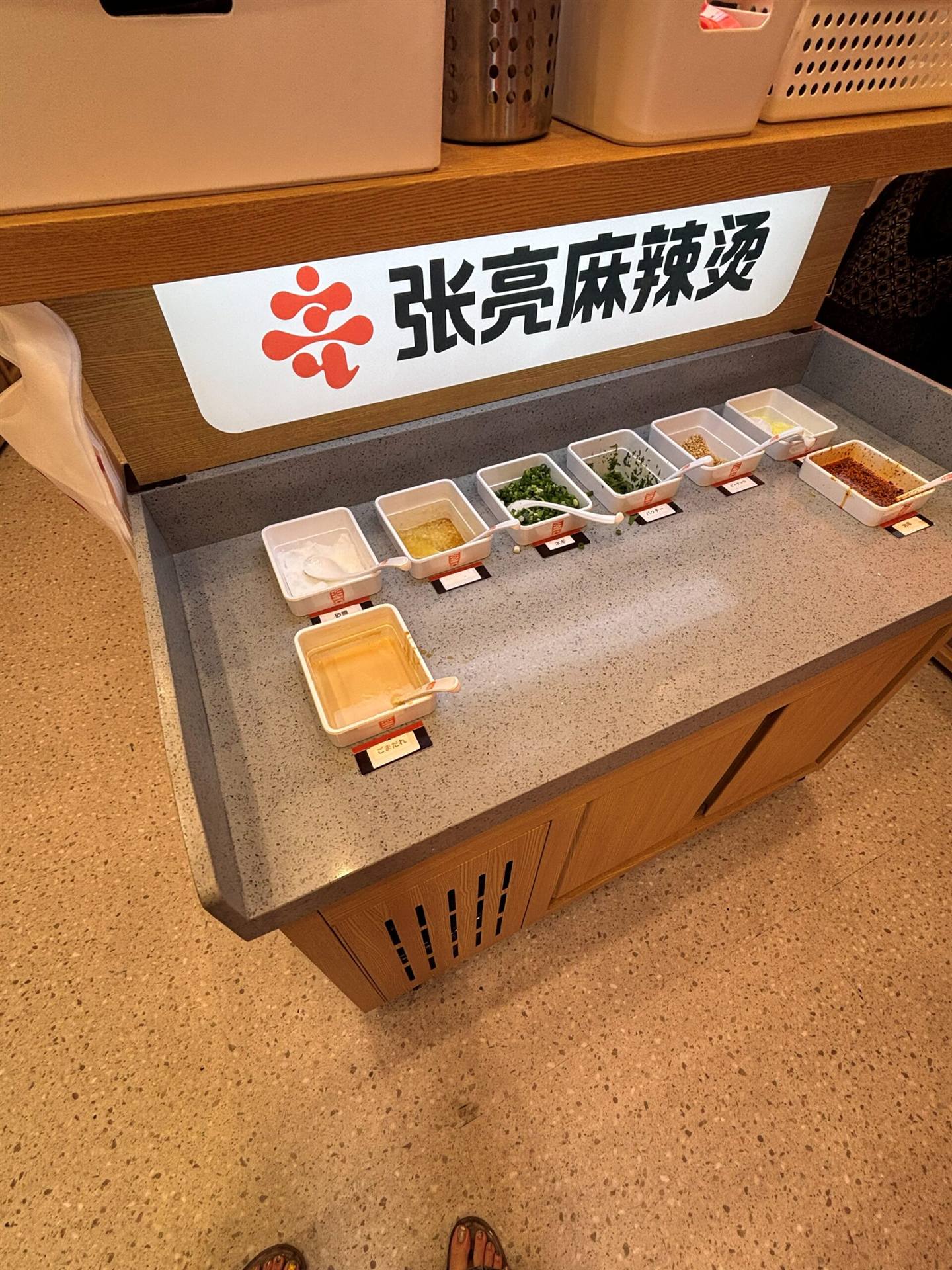張亮麻辣湯のセルフ調味料コーナー、砂糖・ごまだれ・ネギ・パクチー・辣油などが並ぶ
