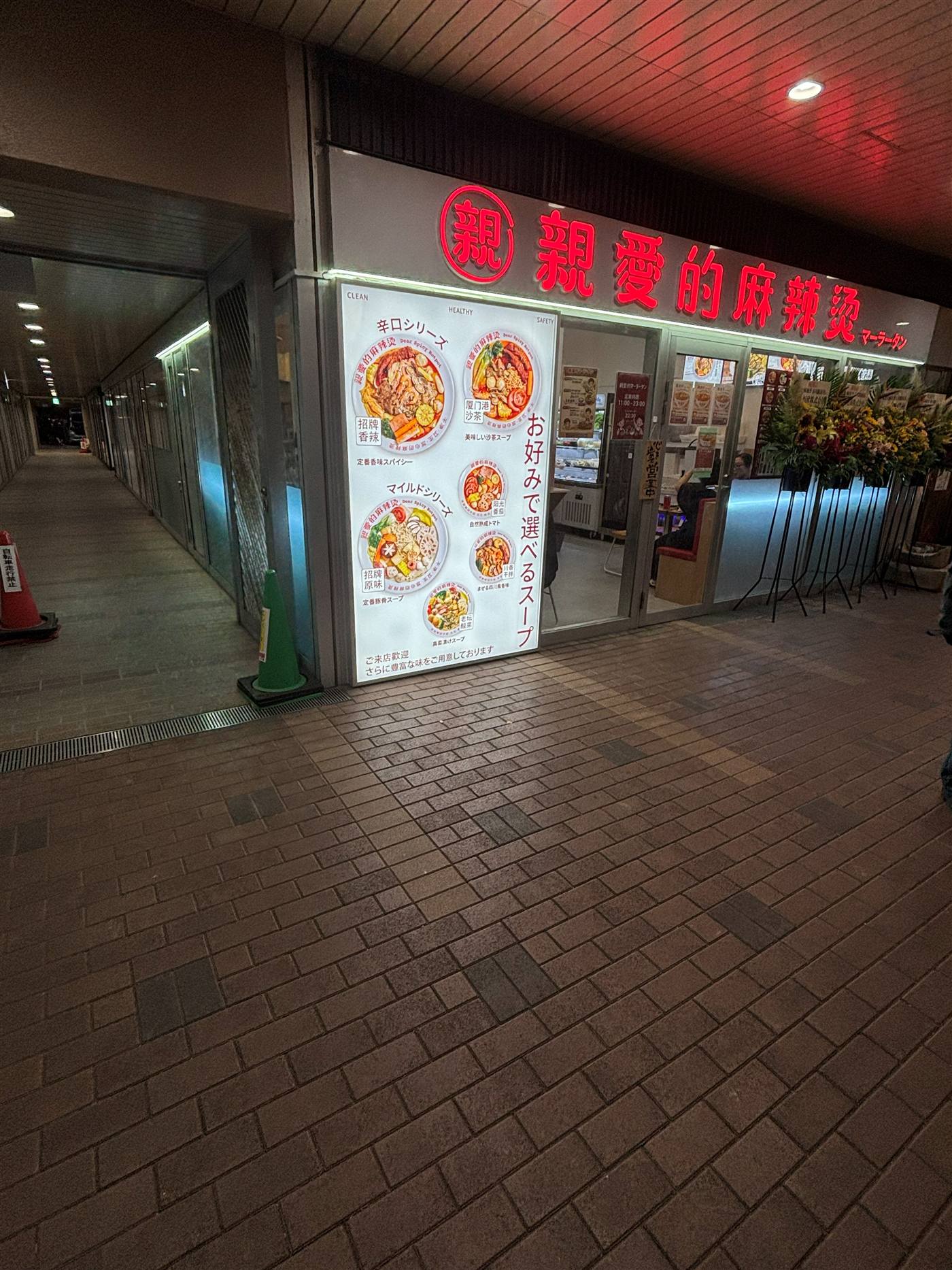親愛的麻辣湯 市川駅前店の外観、開店祝いの花が並ぶ夜の店頭