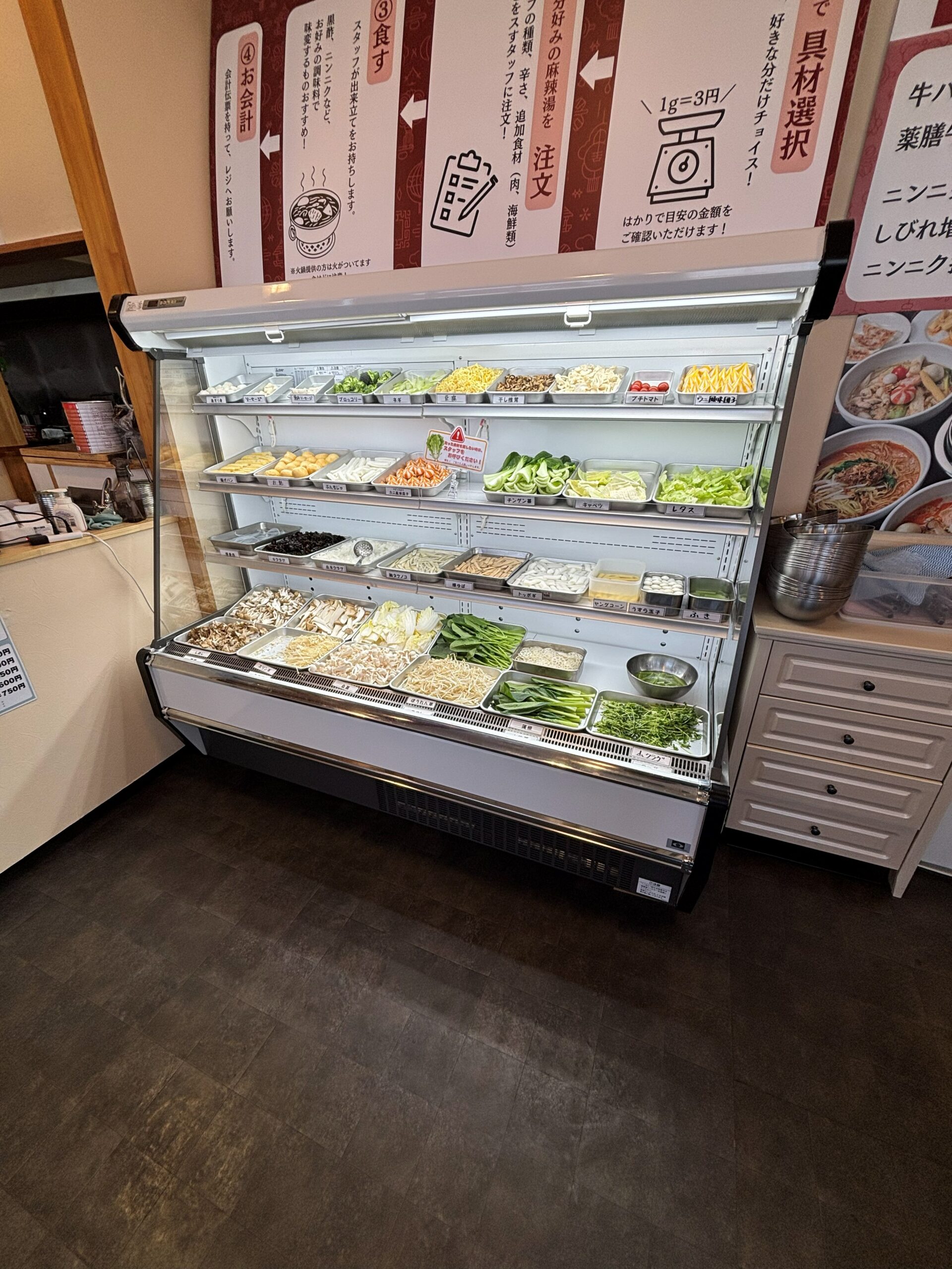 天使担々麺の具材ショーケースと注文の流れの案内(具材1g3円)